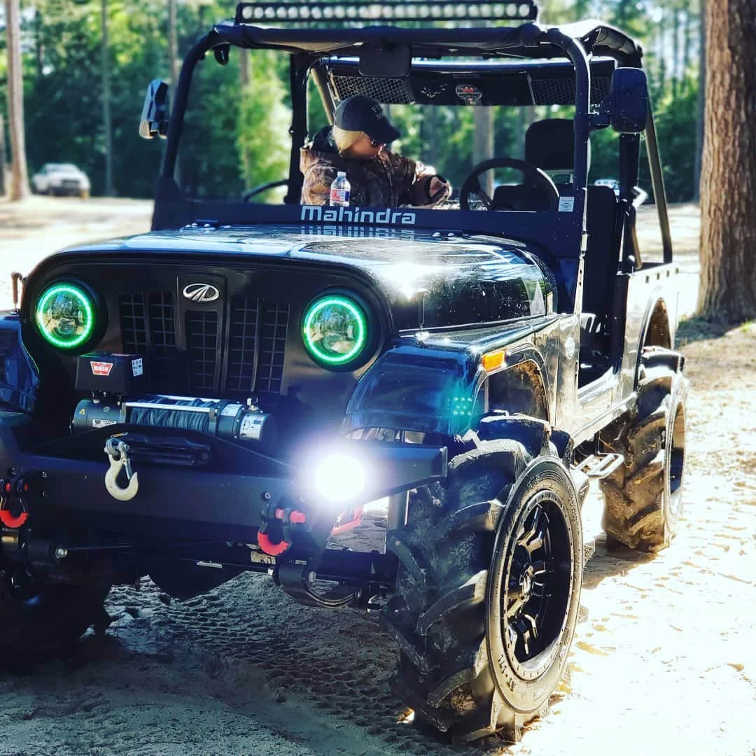 Customized Mahindra Roxor with glowing green headlights and LED lighting modifications parked on dirt road.