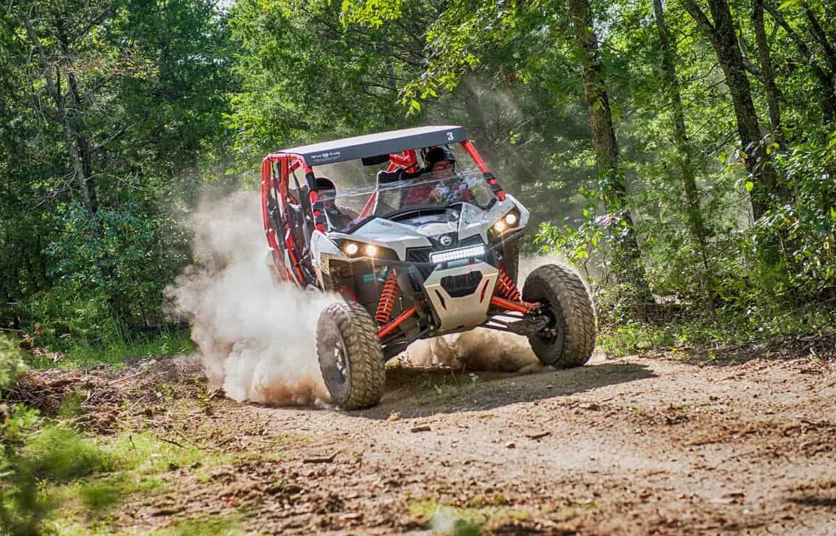 Red and white rally car kicks up dust on forest dirt track during Ride for America rallycross event in Missouri.