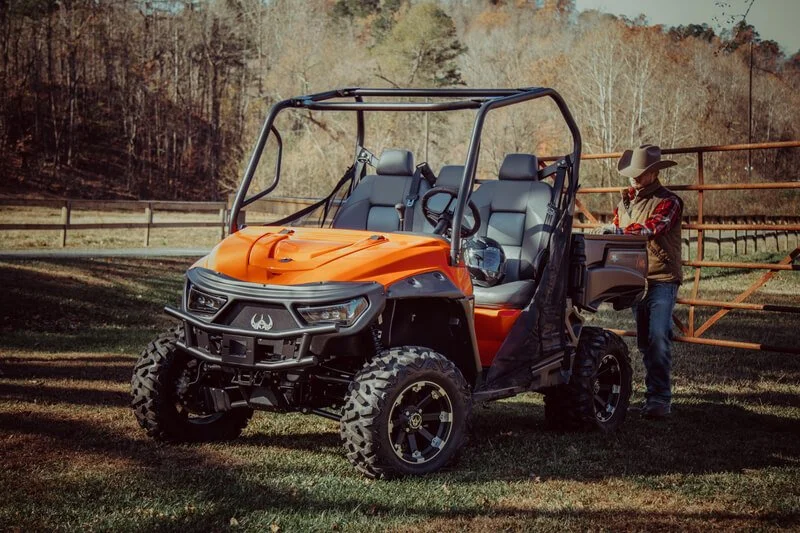 Orange electric UTV parked at rural farm with man standing beside vehicle