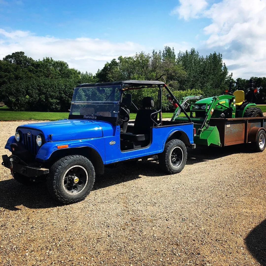 Blue Mahindra Roxor utility vehicle towing green equipment at outdoor summer event display