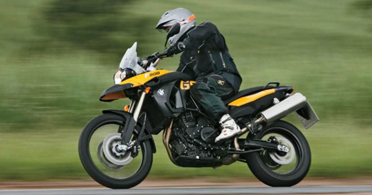Rider on yellow and black dual sport motorcycle in motion on paved road with blurred green background