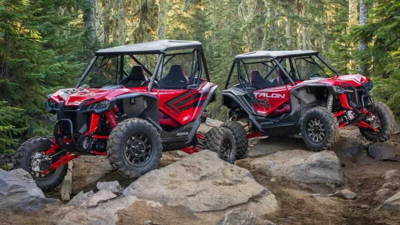Two red Honda Talon side-by-side UTVs parked on rocky terrain in forest