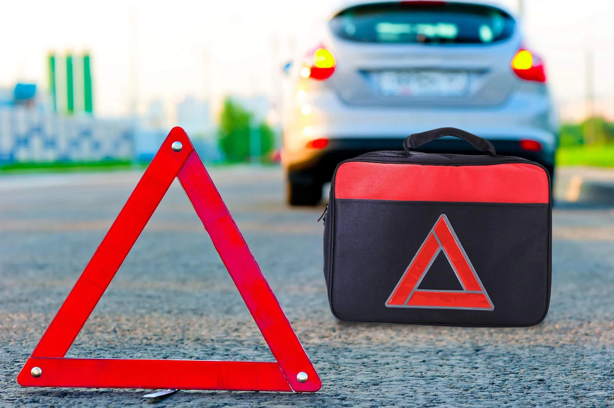Red warning triangle and emergency kit bag on road with disabled car in background
