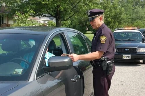 Police officer conducting traffic stop with driver at vehicle window during daytime road check