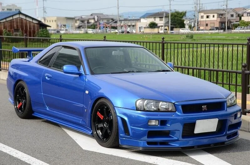 Blue Nissan Skyline GT-R R34 sports car parked outdoors, iconic Japanese performance vehicle subject to US import