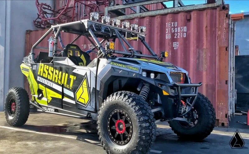 Bright yellow and black Polaris General UTV with roll cage and aggressive graphics parked at industrial yard for NORRA 1000