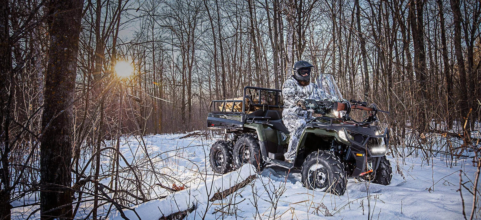 Six-wheeled UTV driving through snowy forest terrain with bare trees and winter landscape visible