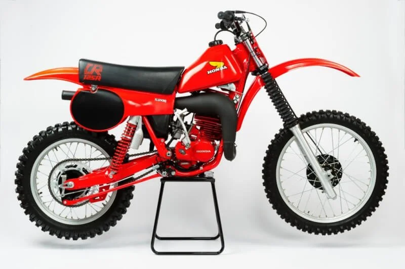 Red vintage dirt bike displayed on stand, showcasing classic 1970s motocross styling and design excellence