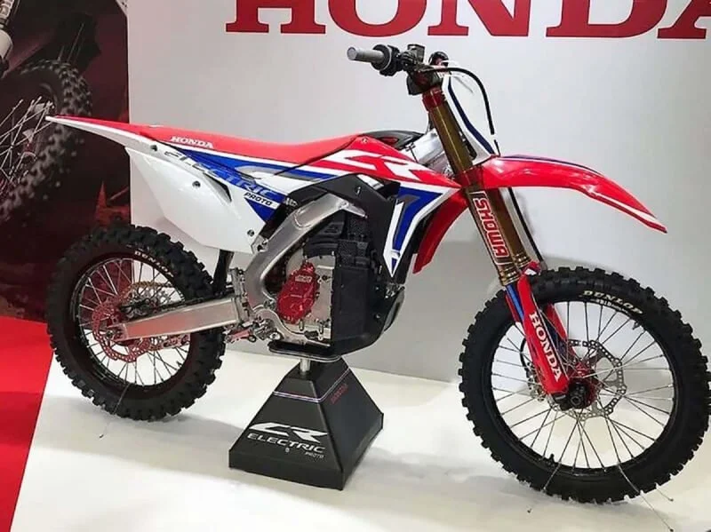 Honda CR Electric dirt bike display model in red, white, and blue on stand at motorsports event