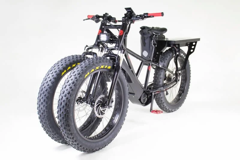 Black three-wheeled electric dirt bike with oversized fat tires and cargo rack displayed against white background
