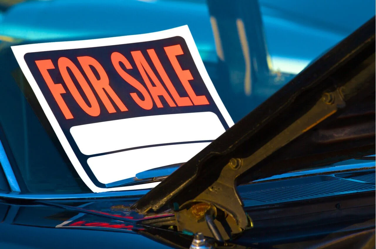 Illuminated for sale sign on blue car windshield, representing vehicle lien and ownership complications when selling a car.