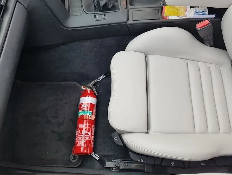 Red fire extinguisher mounted on truck cab floor next to white seat for vehicle safety emergencies