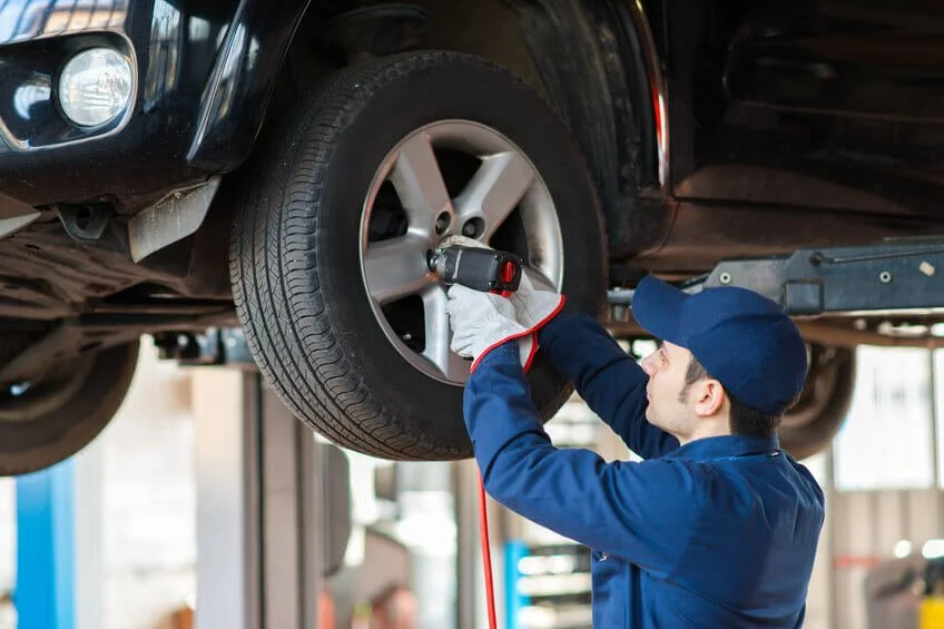 Mechanic in blue uniform inspecting vehicle wheel and tire during pre-purchase car inspection at auto shop