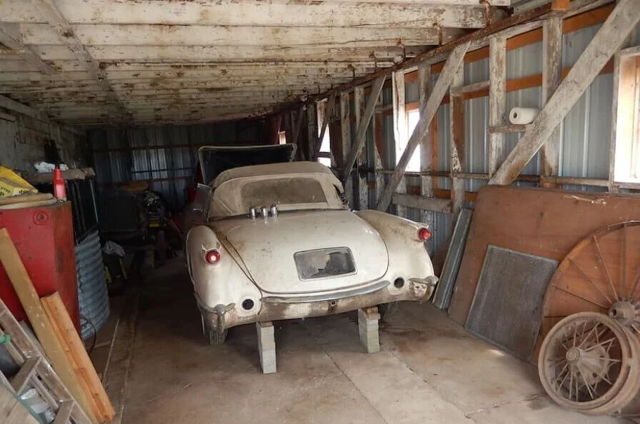 Rare vintage sports car discovered in dusty barn garage, surrounded by old car parts and collectible automotive memorabilia