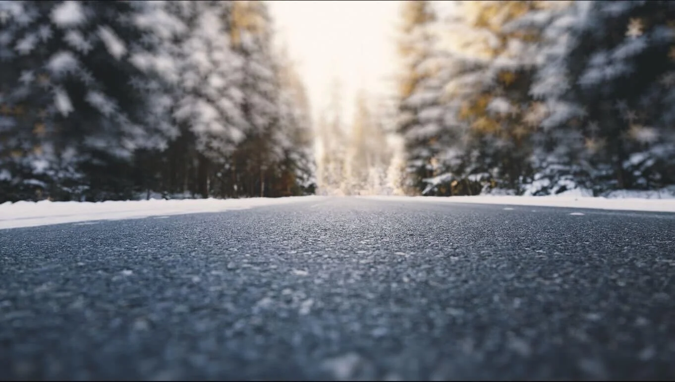 Snow-covered road stretching through winter forest with icy asphalt surface for heated windshield wipers