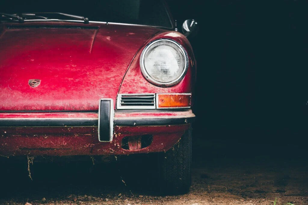 Vintage red Porsche barn find with weathered patina and round headlight showcasing classic automotive restoration potential