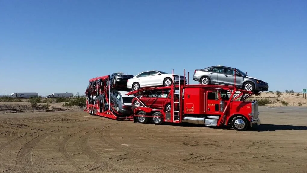 Red auto transport truck carrying multiple vehicles on desert highway
