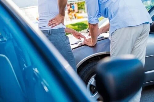 Two men negotiating car sale price at blue vehicle during outdoor inspection and transaction