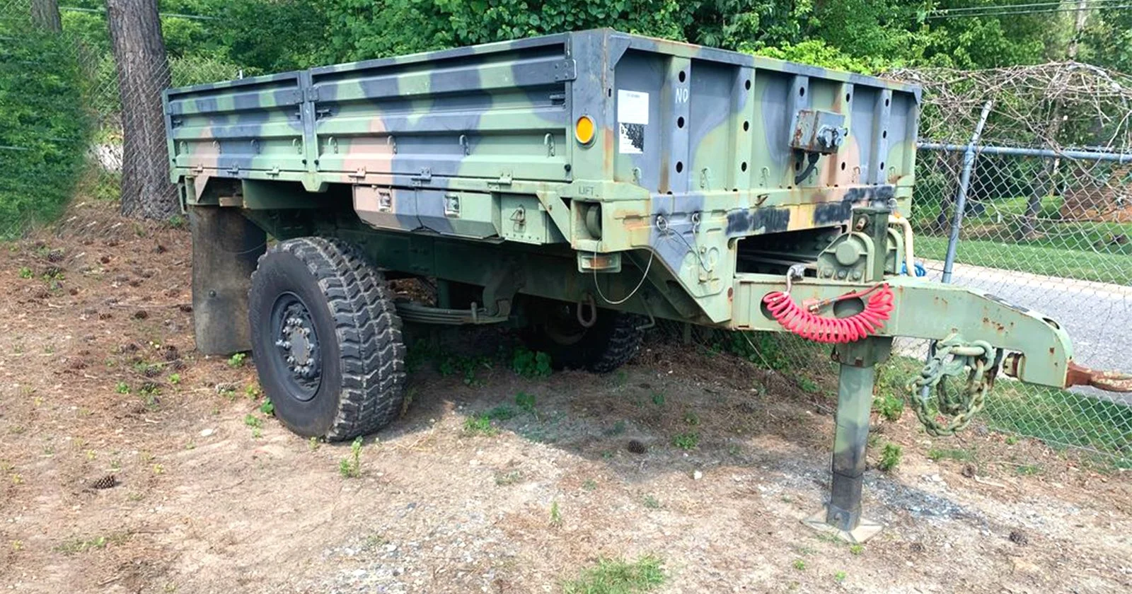 Military XM1082 LMTV cargo trailer with tie-down points parked in wooded outdoor setting for off-road adventures