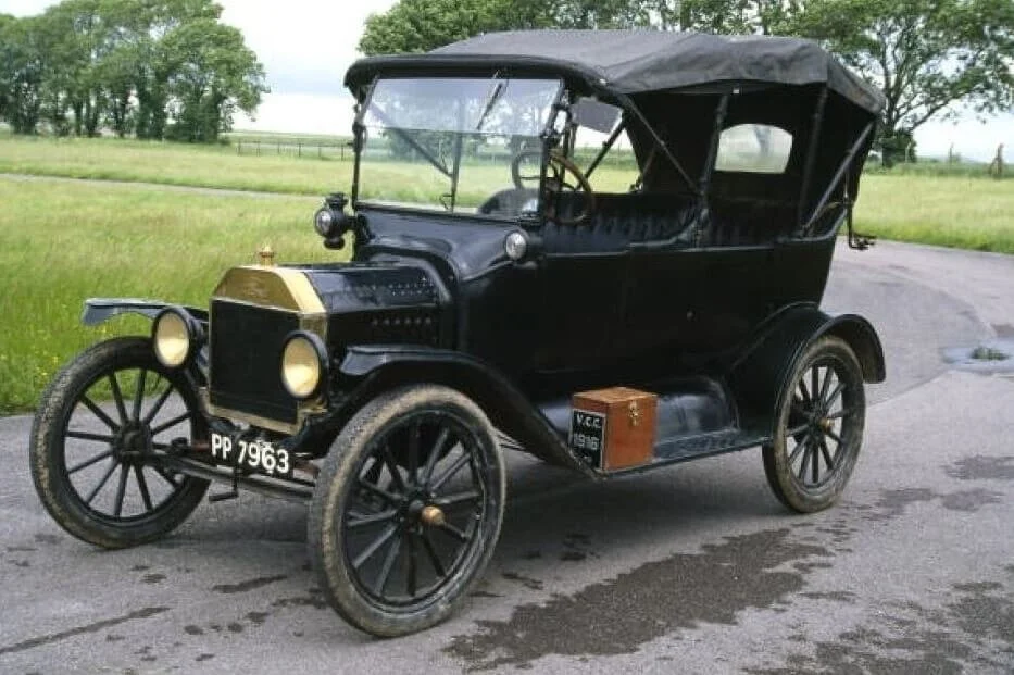Black vintage Model T Ford with convertible top parked on rural driveway, classic car without visible VIN