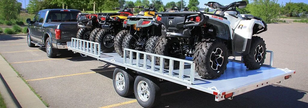 Multiple ATVs and UTVs loaded on white enclosed trailer towed by black pickup truck, demonstrating proper UTV hauling method