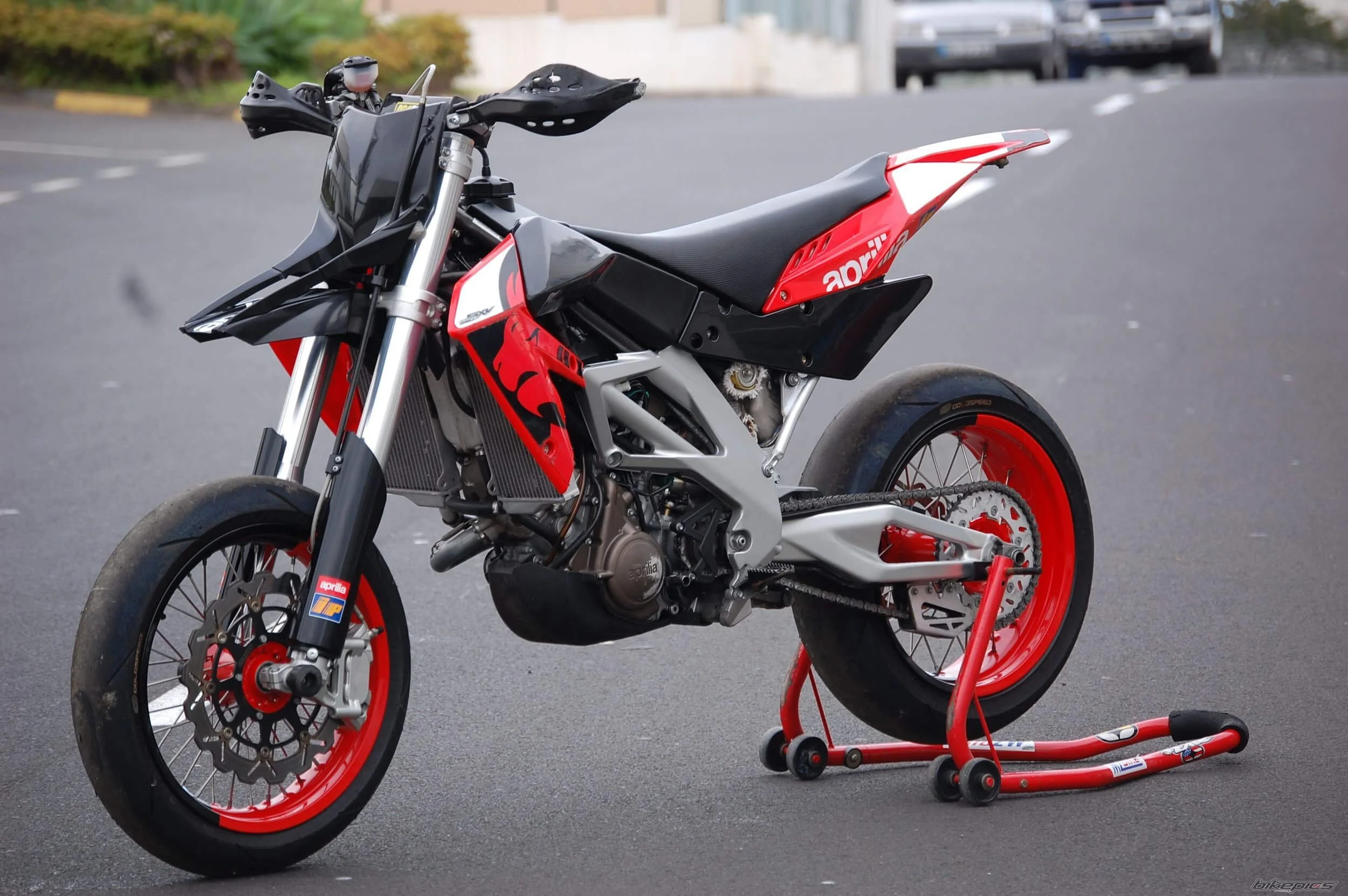 Red and black street legal dirt bike on maintenance stand in parking lot, showcasing factory design.