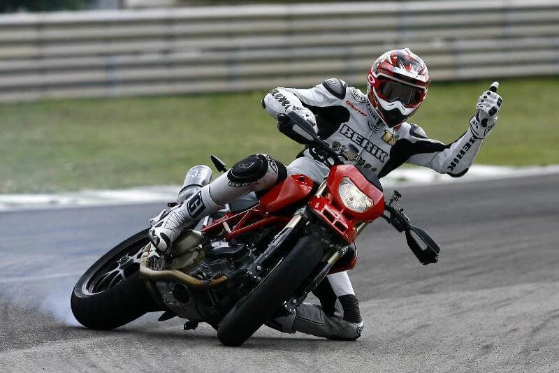 Red supermoto motorcycle leaning into turn on racing circuit with rider celebrating victory