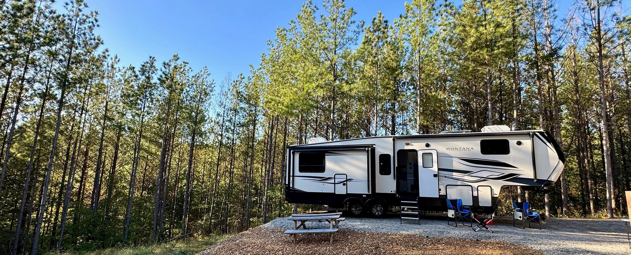 Montana travel trailer parked at forest campsite with picnic table and chairs for RV camping adventure