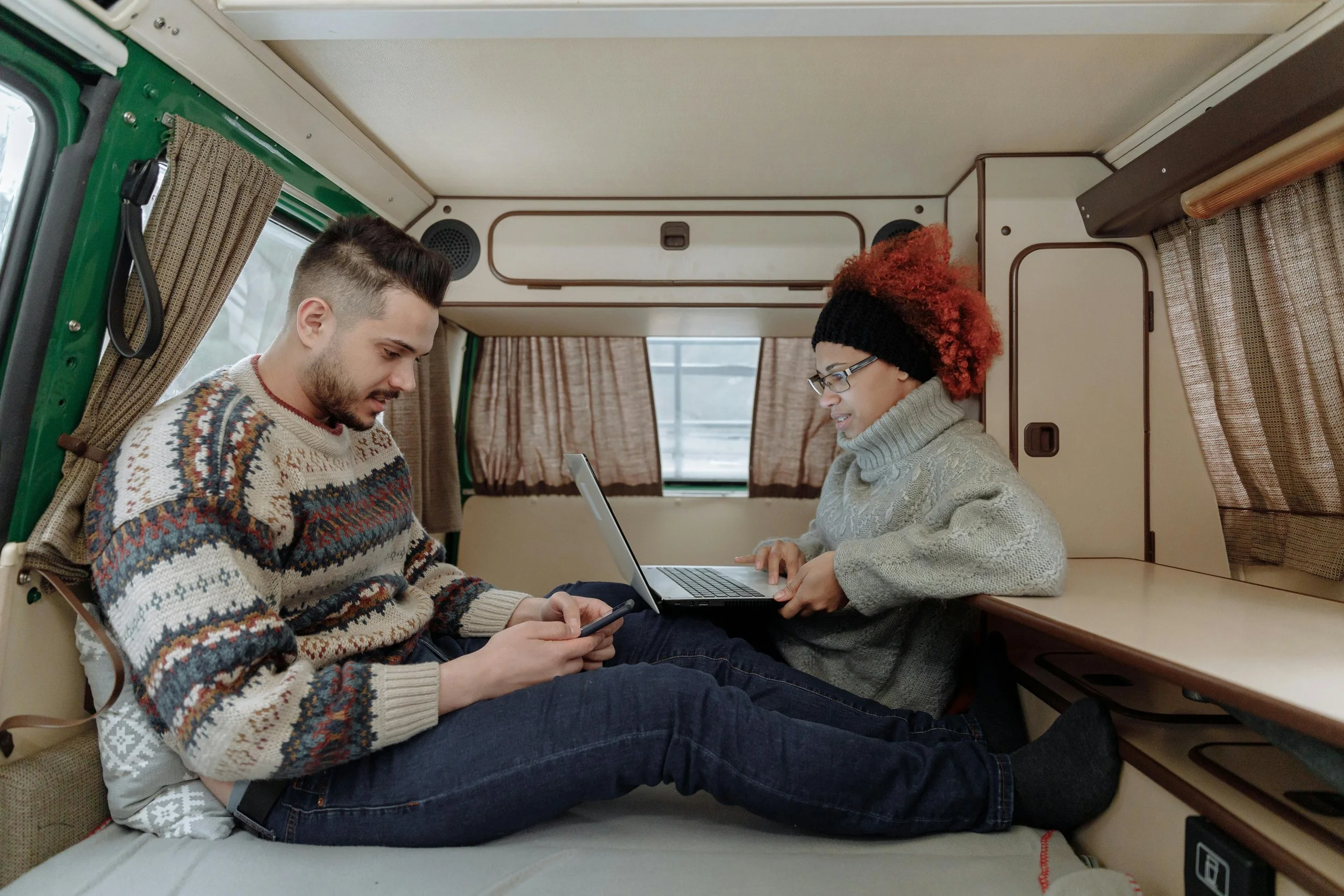 Couple using laptop inside RV camper, planning travel adventures and bucket list goals for new year