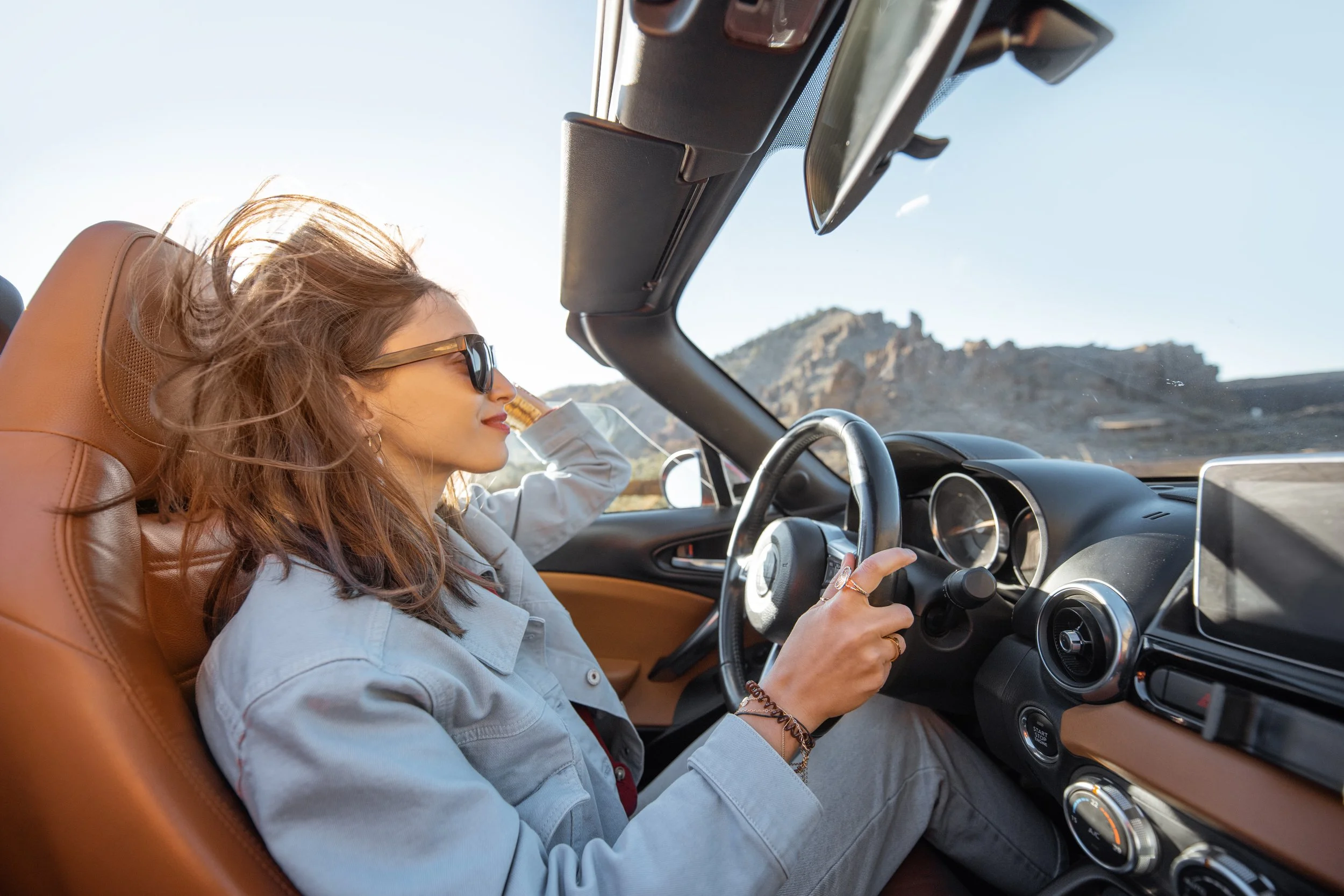 Woman driving convertible car on scenic mountain road with clear sky and landscape view