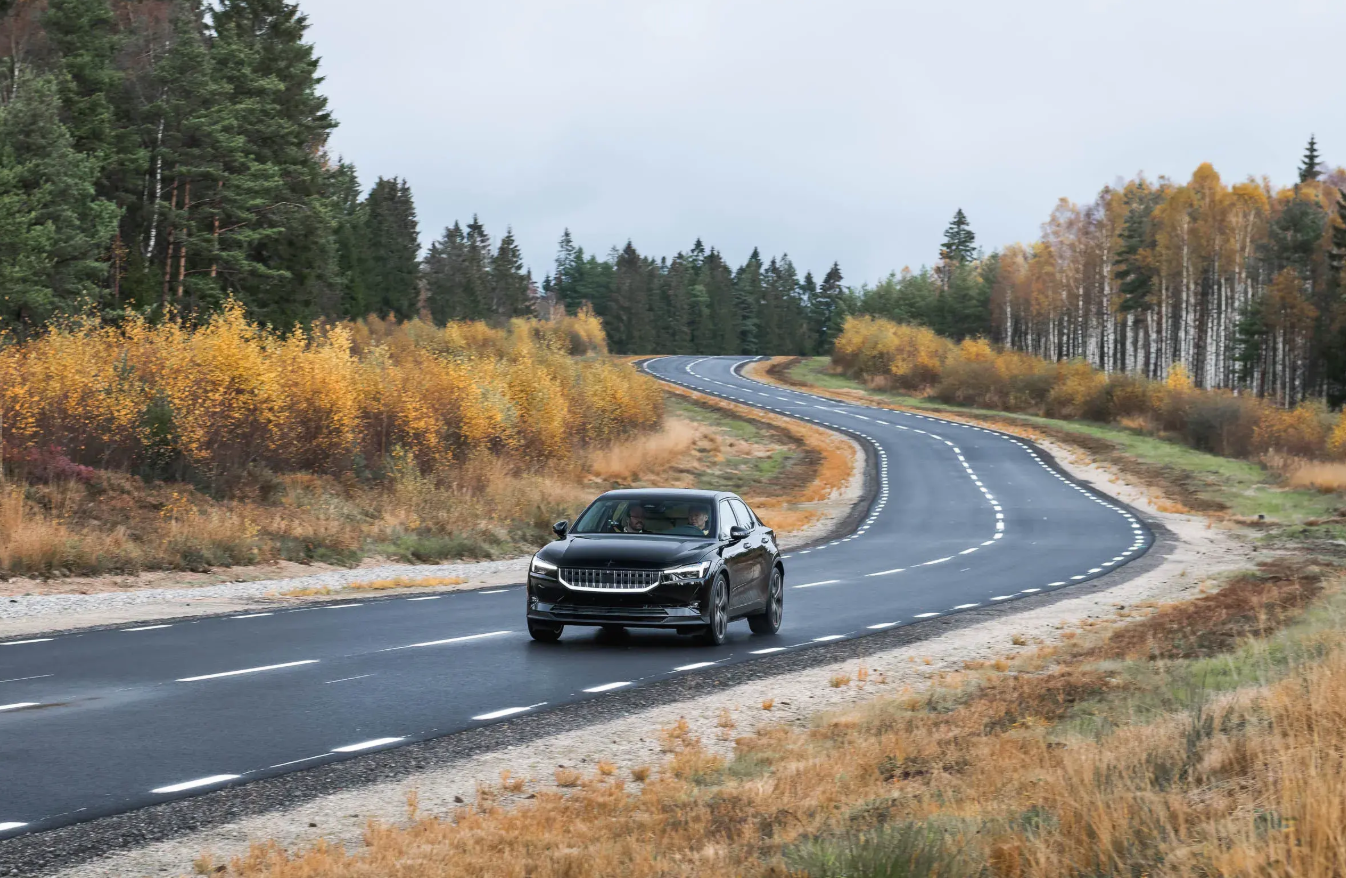 Black elevated SUV driving on curved highway through autumn forest landscape with trees and golden foliage