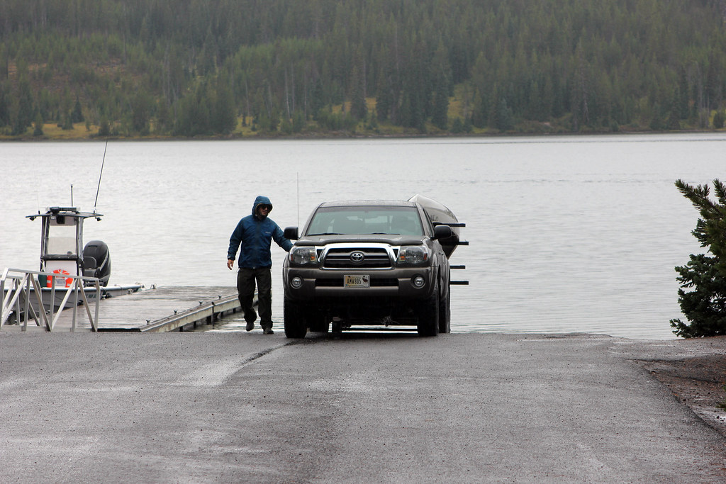 Man loading boat onto trailer at lakeside dock with forest backdrop, Montana outdoor recreation scene