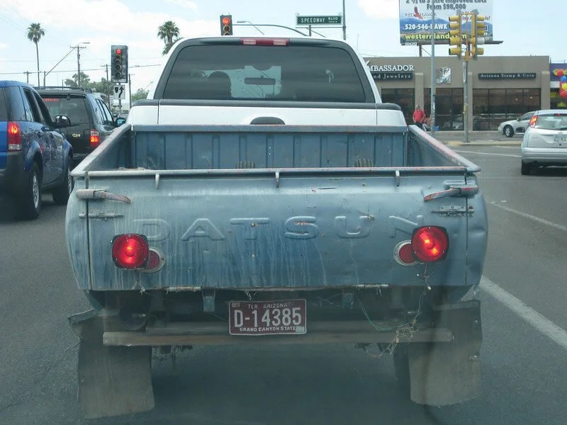 Weathered blue pickup truck bed trailer with white cab frame parked on Arizona street, upcycled utility vehicle