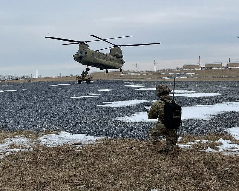 Military CH-47 Chinook helicopter landing near soldier during training exercise on airfield