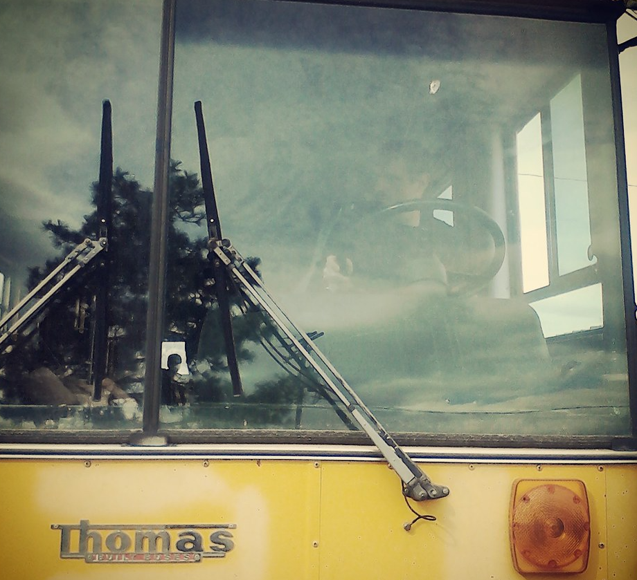 Yellow school bus converted into skoolie RV with open window and antennas against cloudy sky