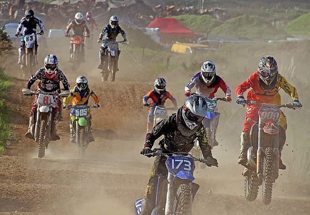 Group of young motocross riders racing on dusty dirt bike track in competitive off-road competition event