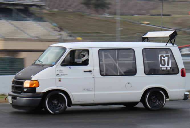 White Dodge van with number 67 racing decals driving on street track, example of street-legal race vehicle