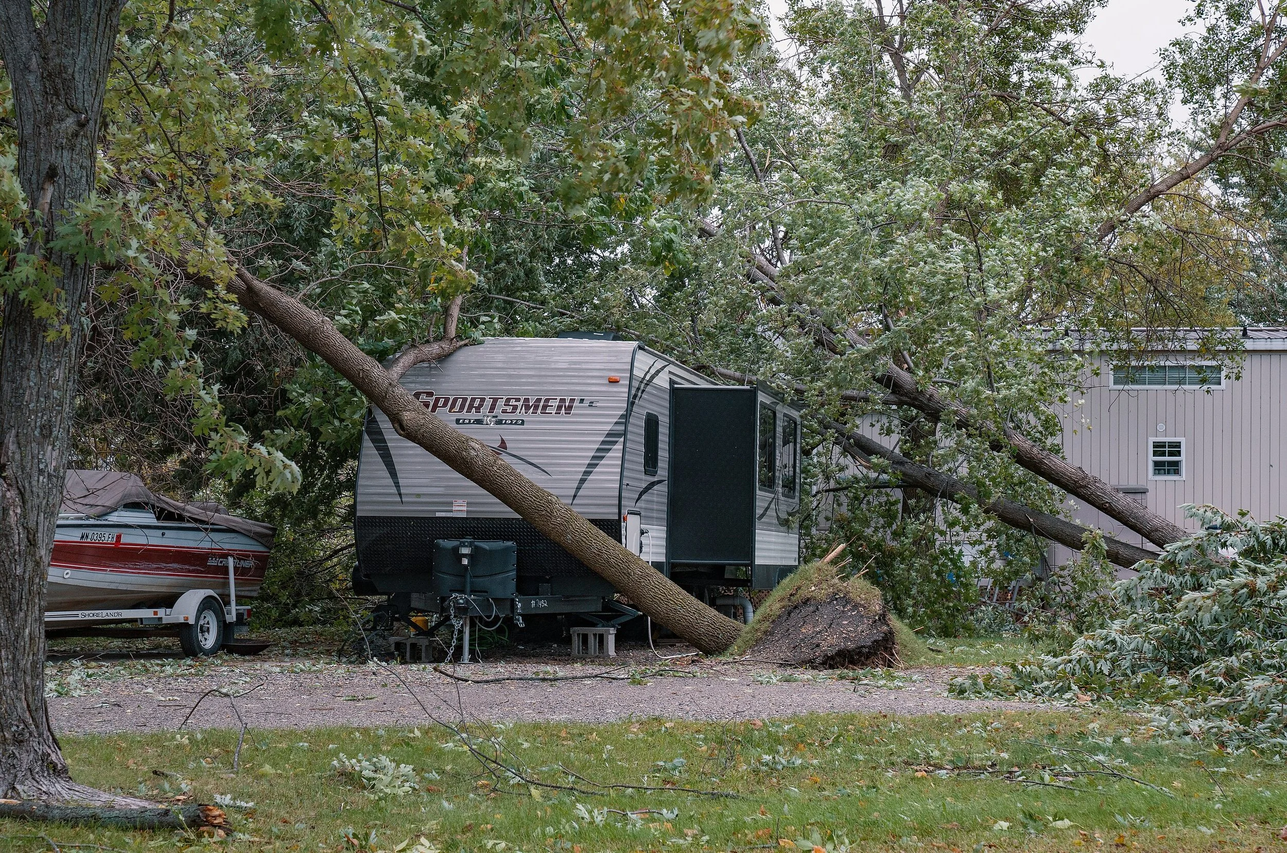 Sportsmen travel trailer damaged by fallen tree in wooded campground, illustrating RV salvage title risks from weather damage