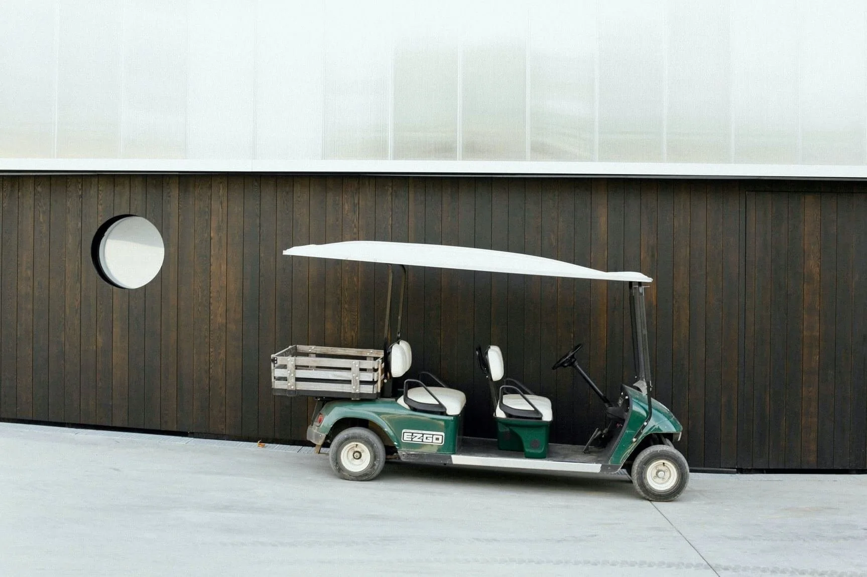Green golf cart with canopy parked against dark wooden building, representing street legal modifications for public road use.