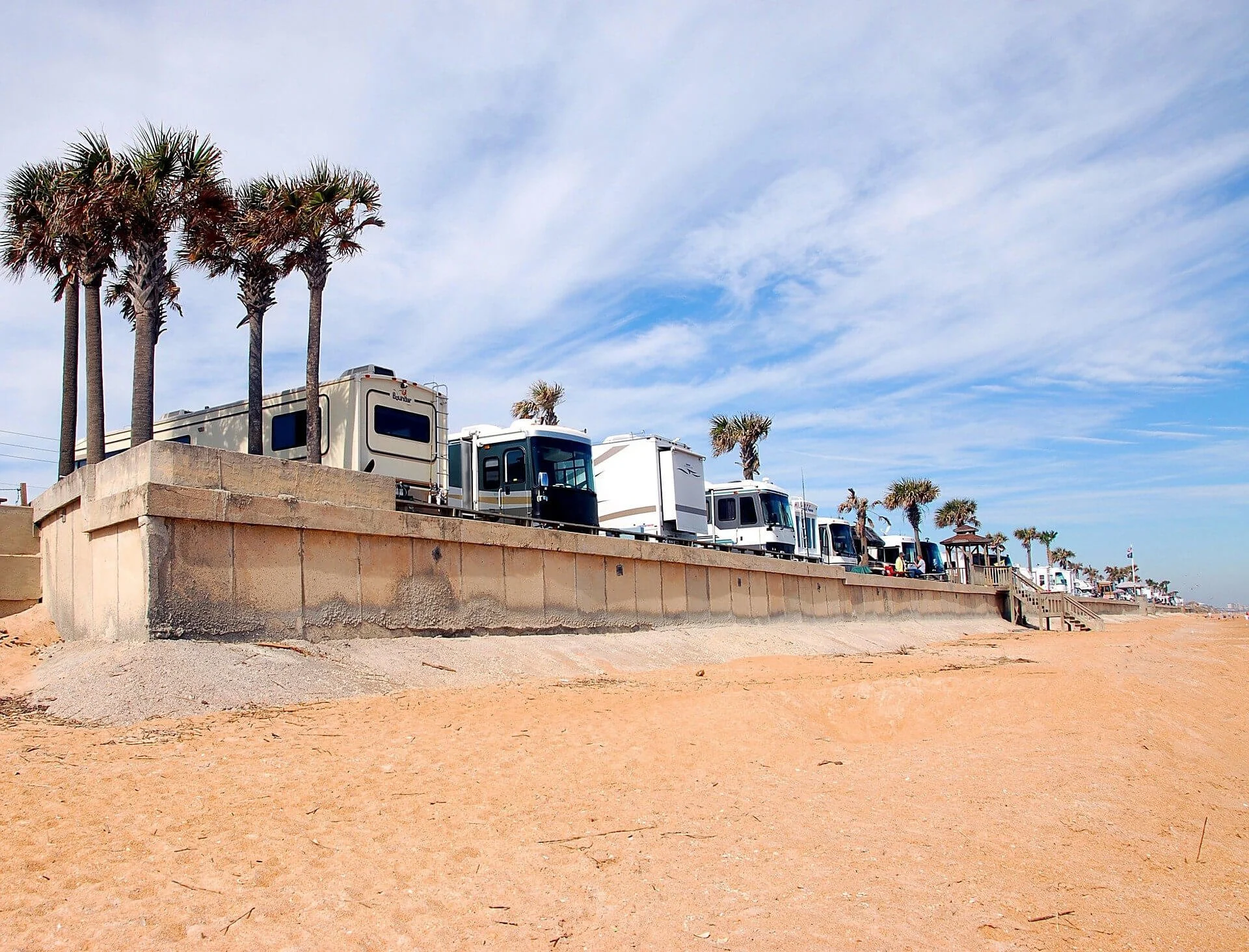 RVs parked on sandy beach with palm trees, illustrating vehicle registration considerations for Canadian travelers in US.