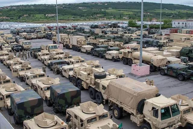 Military surplus cargo trucks and trailers parked in organized rows at large depot facility for overlanding conversion