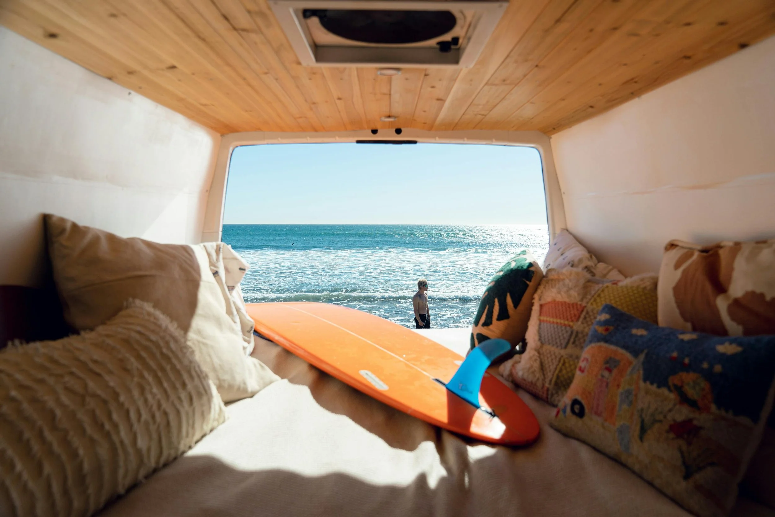 Camper van interior with surfboard parked at beach, showcasing van life adventure and coastal living lifestyle.