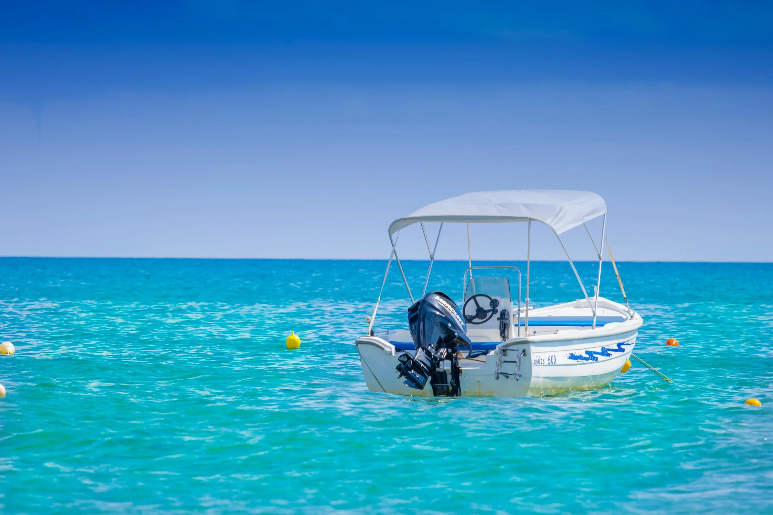 White motorboat with canopy anchored in turquoise Mediterranean waters on clear sunny day