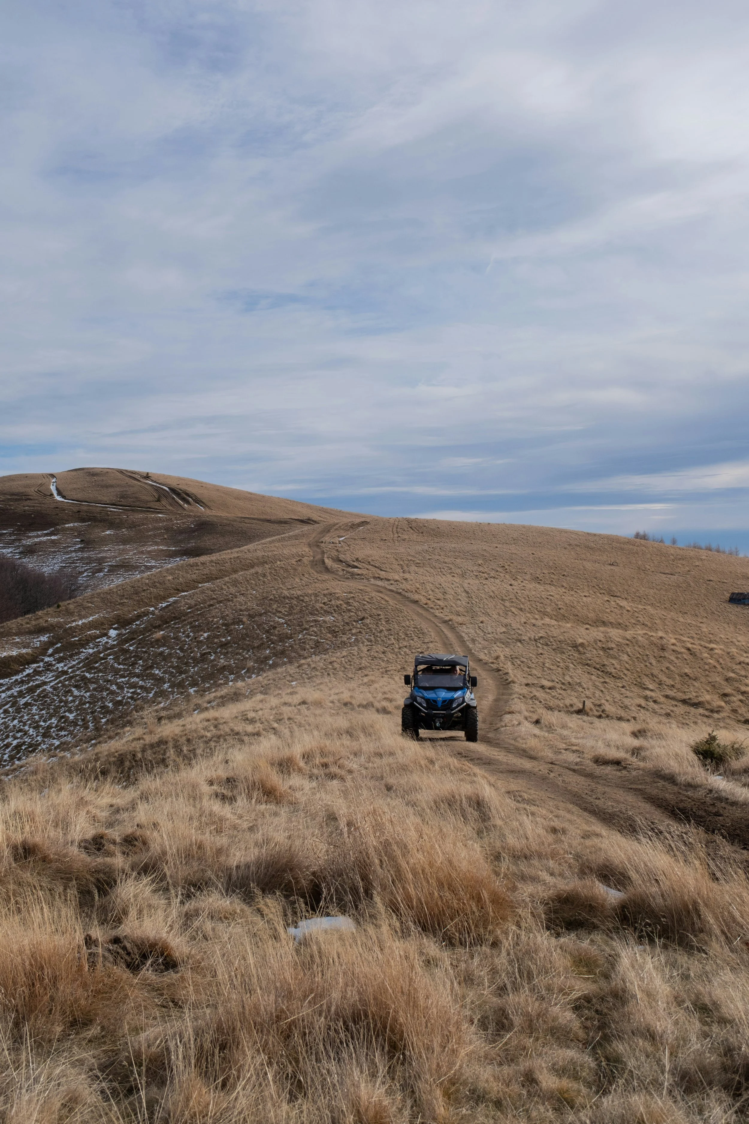 Blue UTV driving on dirt trail across rolling hills in western landscape during daytime