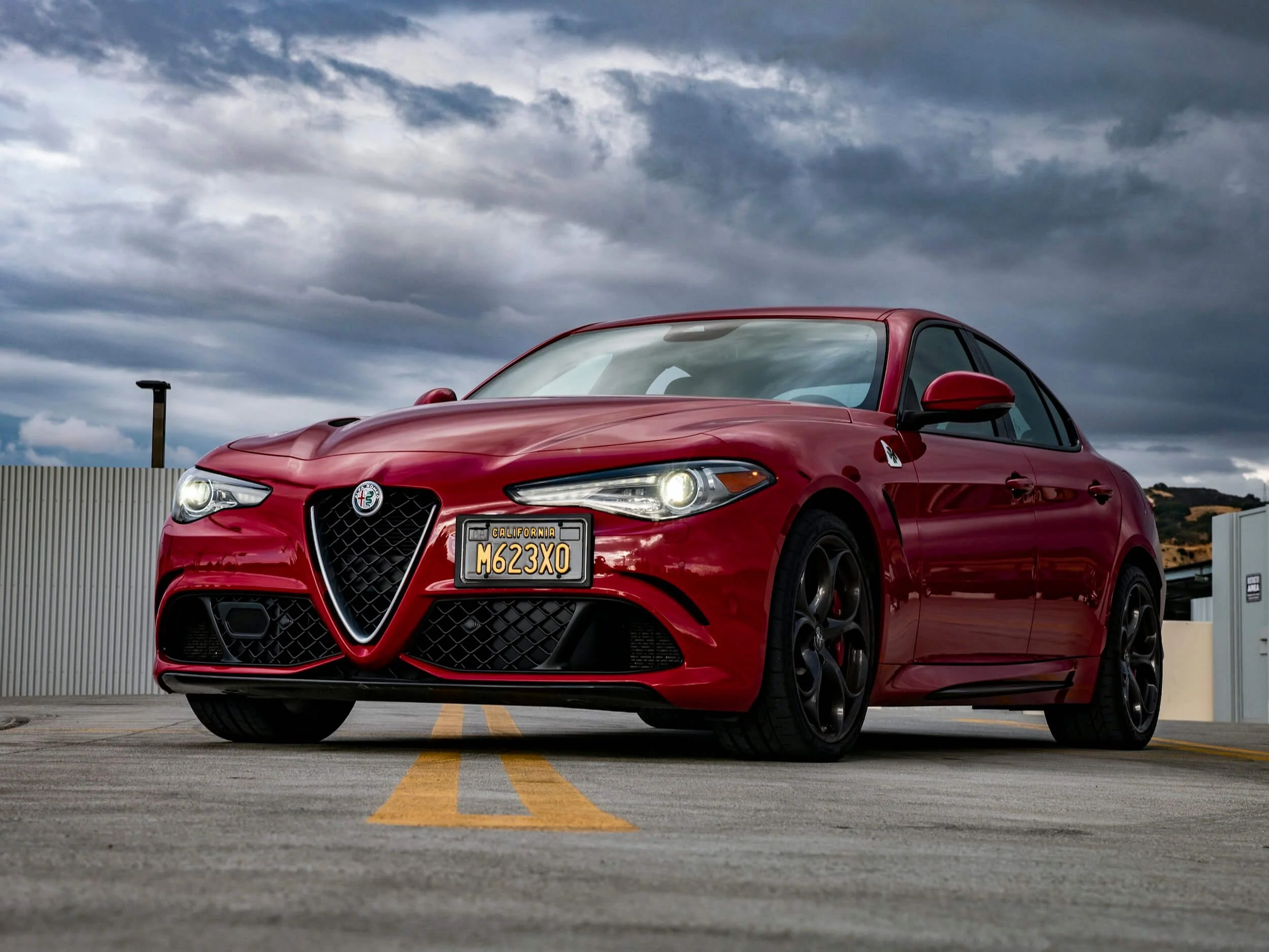 Red Alfa Romeo sedan parked in lot with yellow lines, representing vehicle registration and car-sharing platform