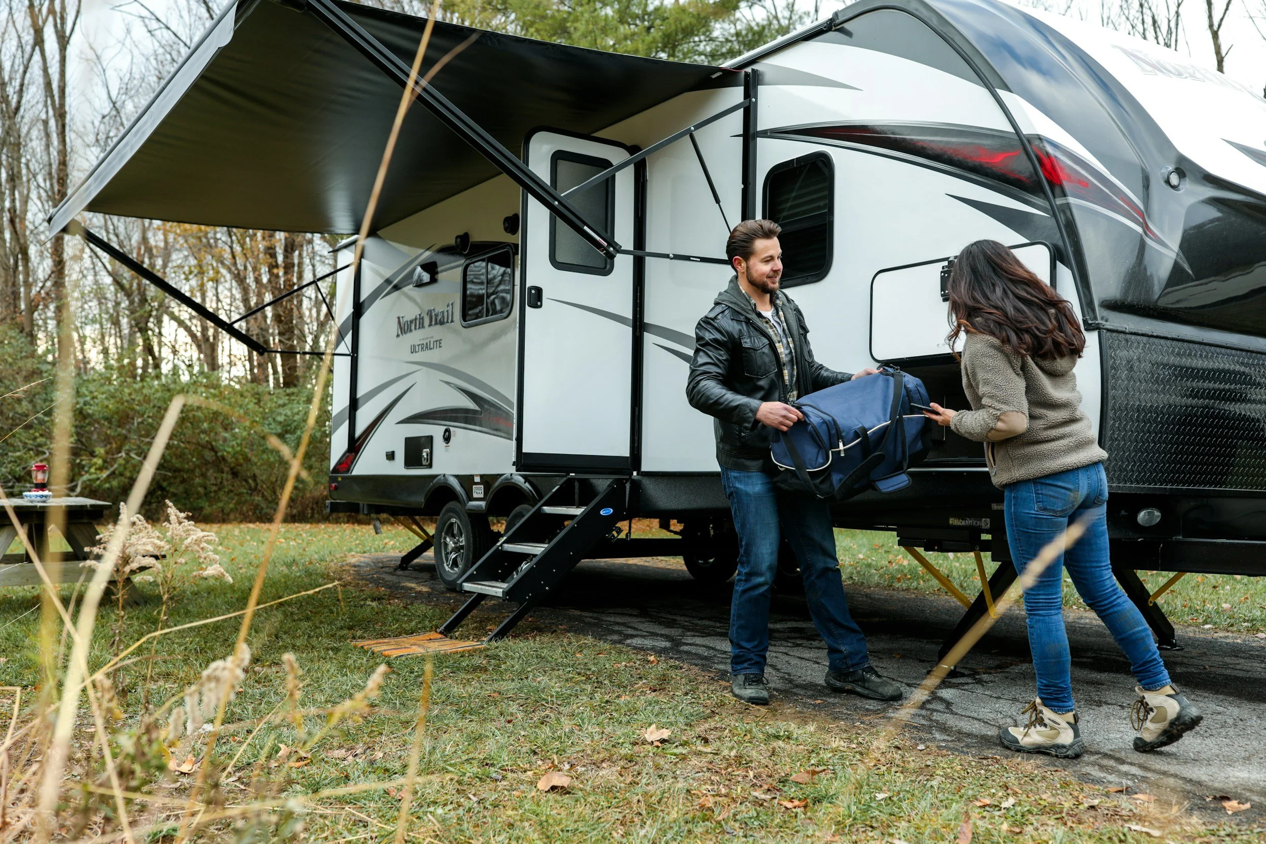 Couple unloading gear from white North Trail travel trailer at campsite, demonstrating RV weight management and towing safety