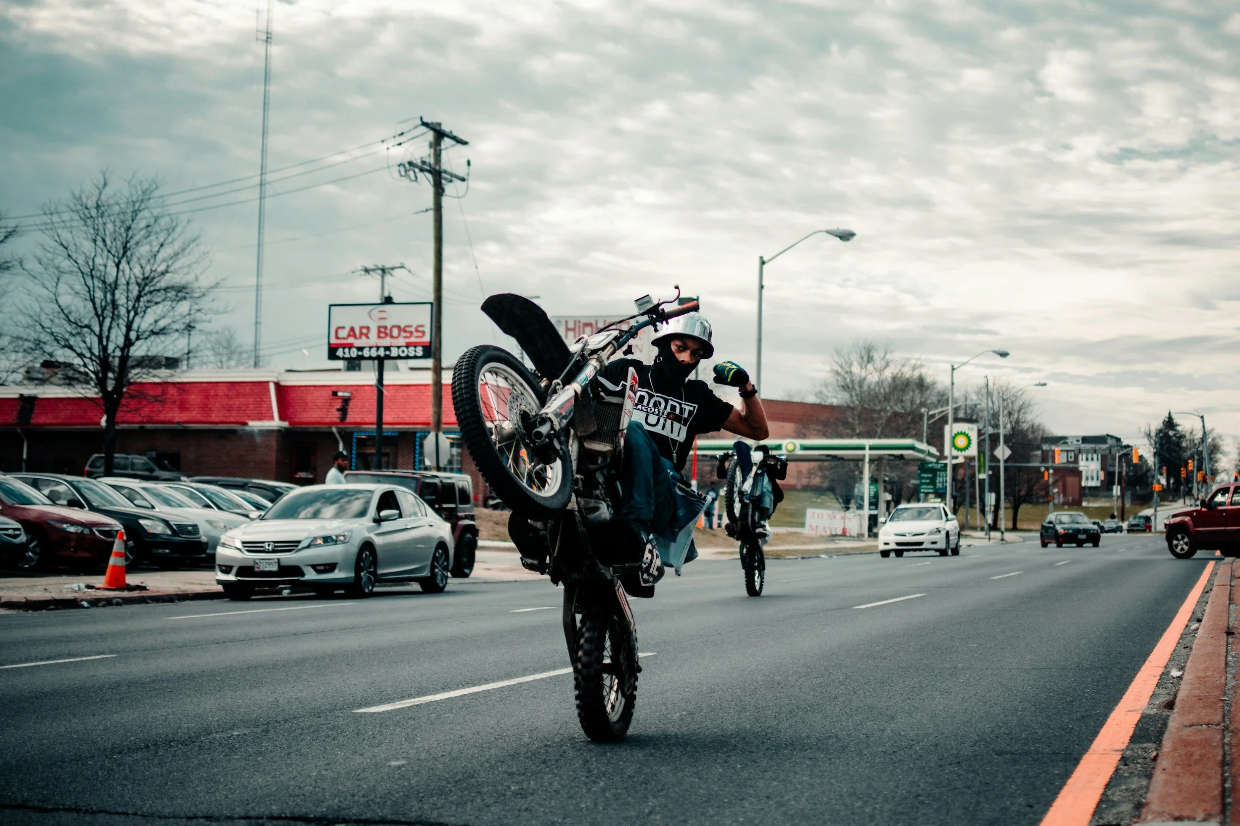 Dirt bike rider performing wheelie on street-legal two-stroke motorcycle downtown urban area.