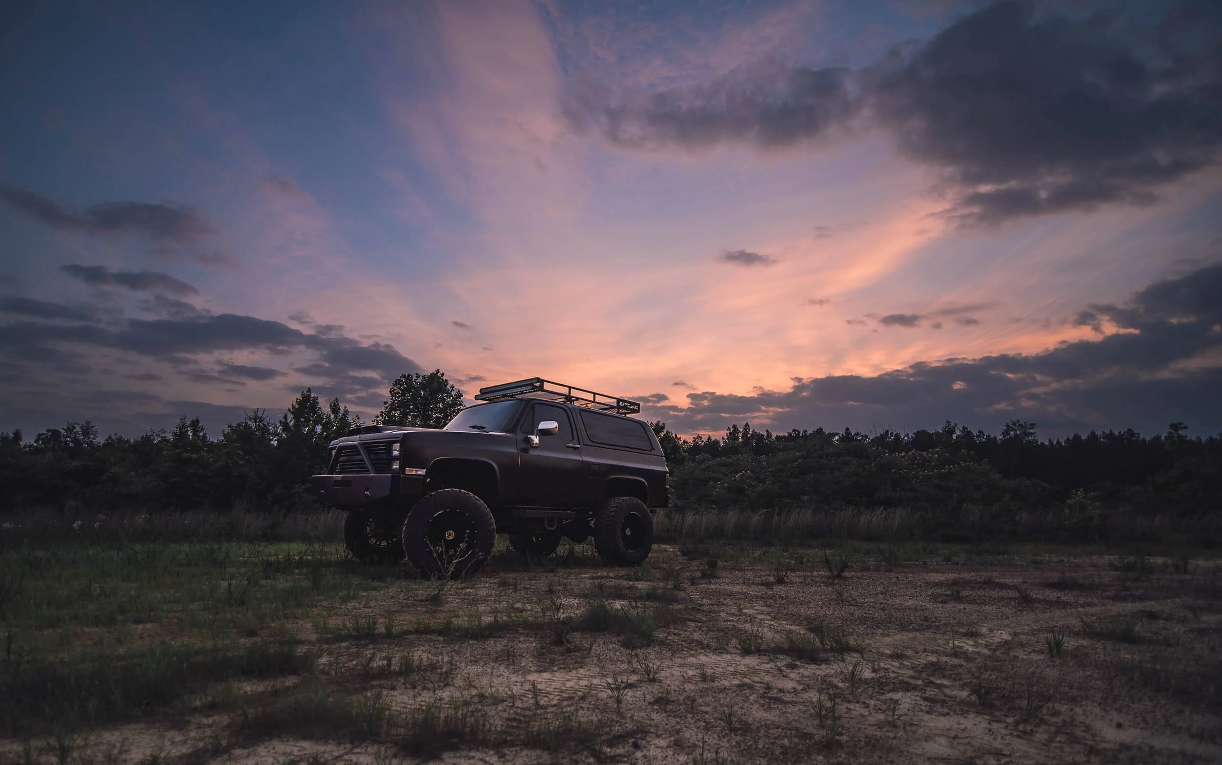 Modified SUV with roof rack parked in desert landscape at sunset