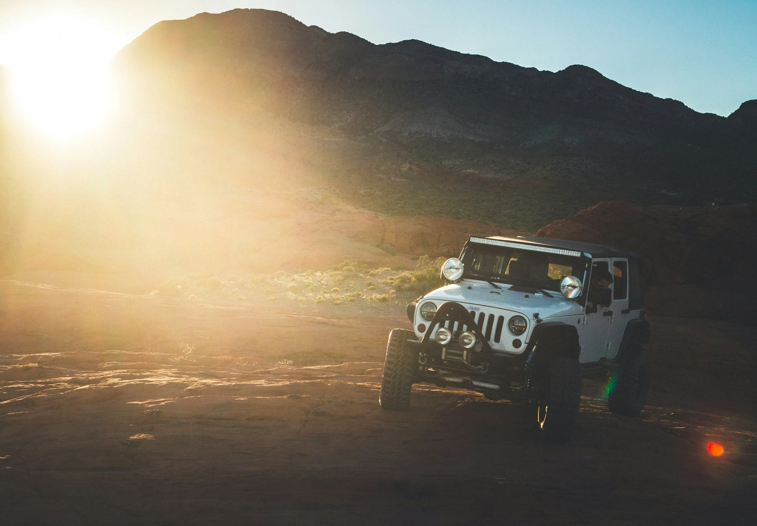 White Jeep Wrangler navigating rocky mountain terrain at sunset during off-road adventure in Montana wilderness