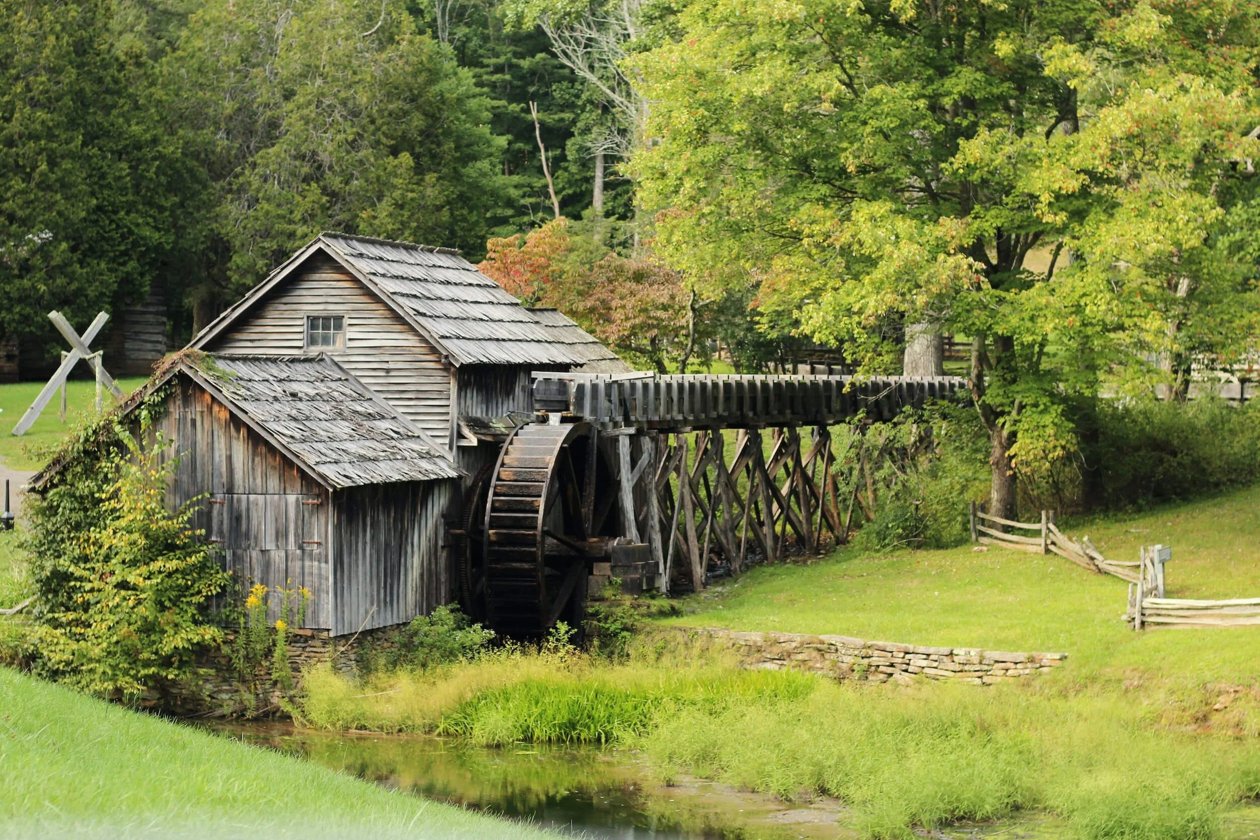 Historic wooden water mill with large wheel beside stream in rural Virginia countryside setting